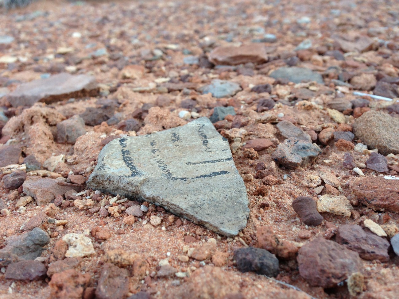 a small piece of pottery with white and black decorations among rocky debris