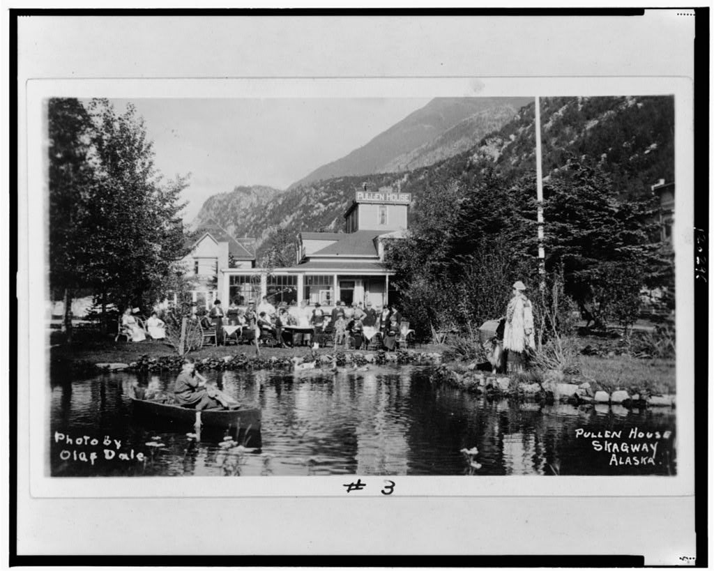 A gran house with a pond in the front and a social gathering on the lawn