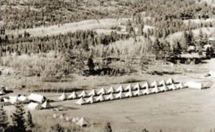 Two rows of tents at the bottom of a hill covered in evergreen trees