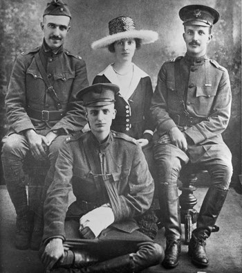 Three men in military uniforms and one woman in dress and large hat sit for a photo.