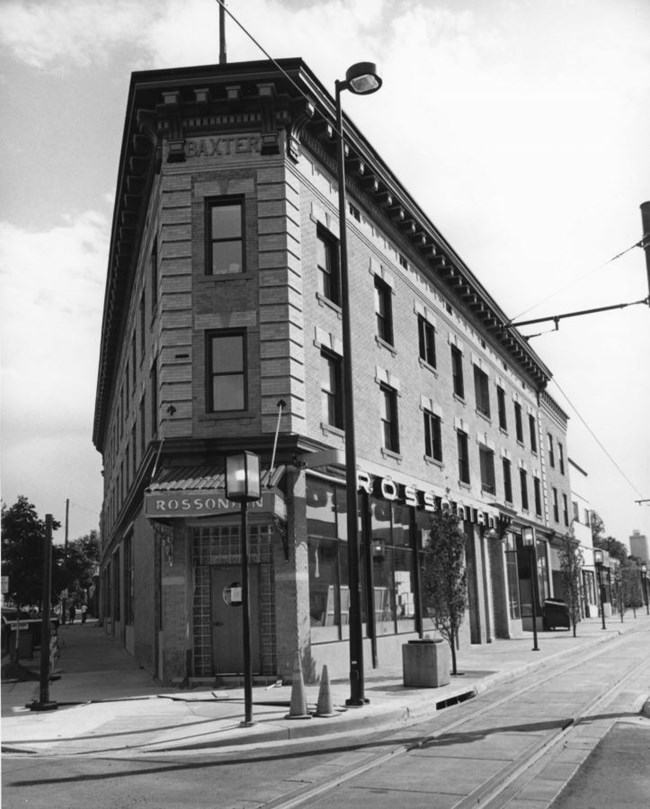 corner entrance façade of a three-story store front building on the corner of an intersection
