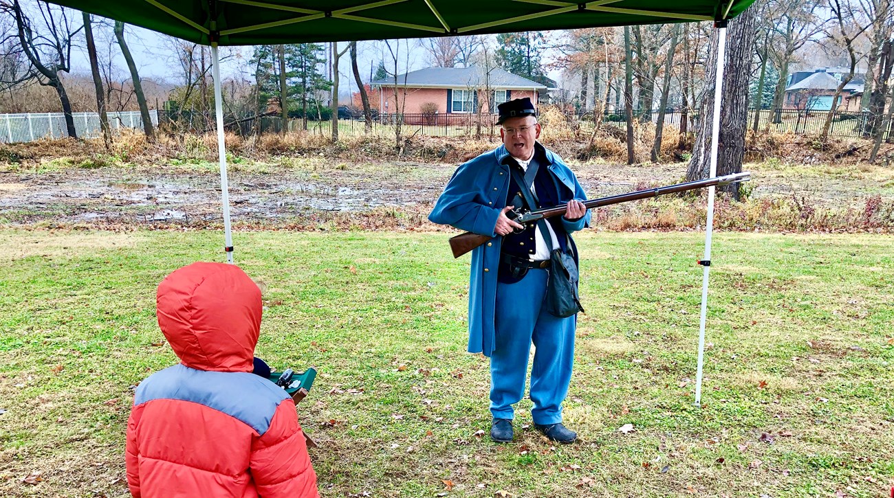 Man dressed as a Union Civil War private stands, holding a long rifle as waist height.