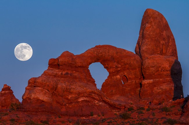 An arch formation at Arches National Park glows under the light of the full moon.