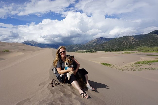 Susan sitting on a sand dune with her dog Smokey at Great Sand Dunes National Park