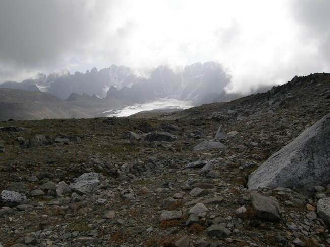 Image of rocky slope with high peaks and snow in background.