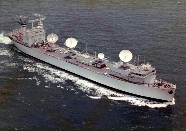 A ship underway with four large communication dishes mounted.