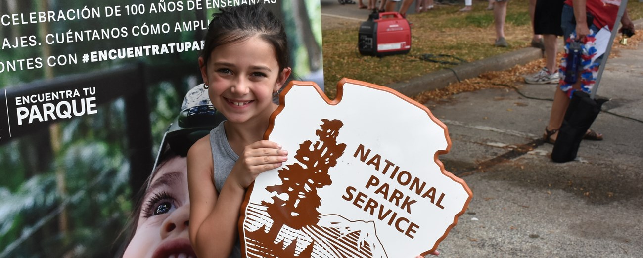 Child holding up a wooden NPS arrowhead logo