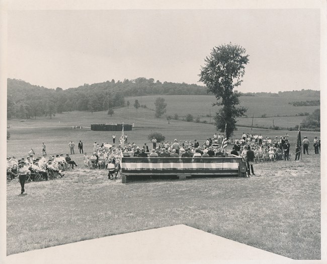 A dedication ceremony with Fort Necessity in the background surrounded by acres of mowed grass
