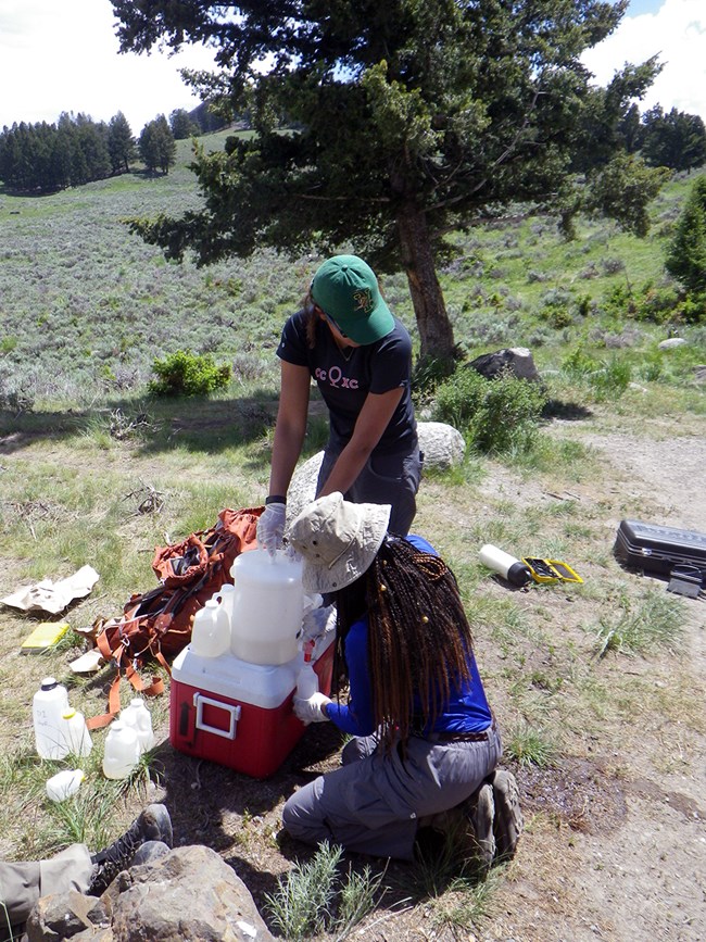 two scientists filling small water bottles from a larger bottle