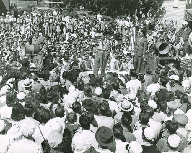 Black and white photo of a crowd with two men standing above with an American flag