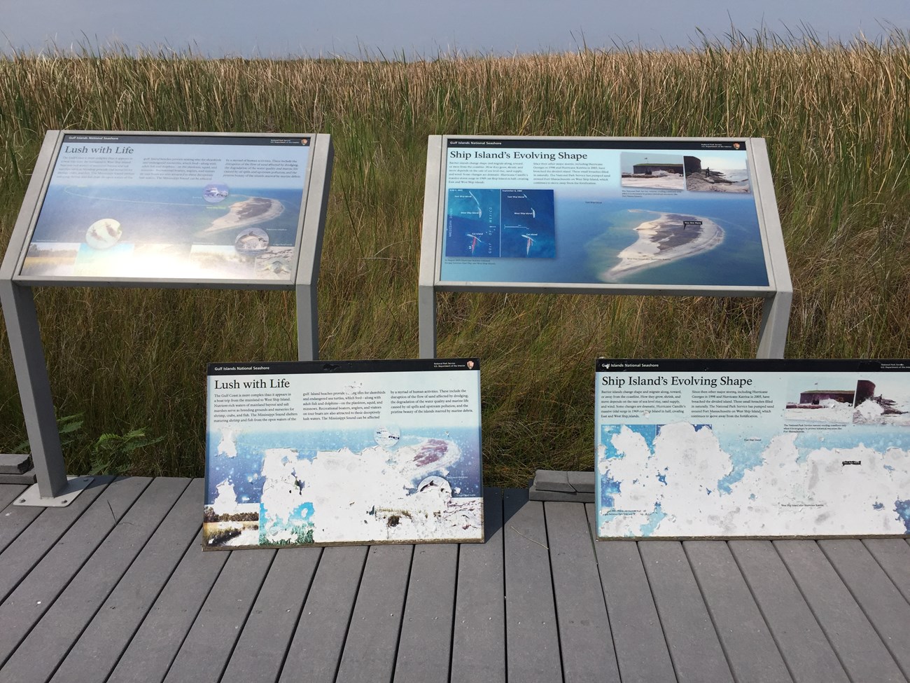 Two sun-damaged wayside panels lean against frames holding the new wayside panels.