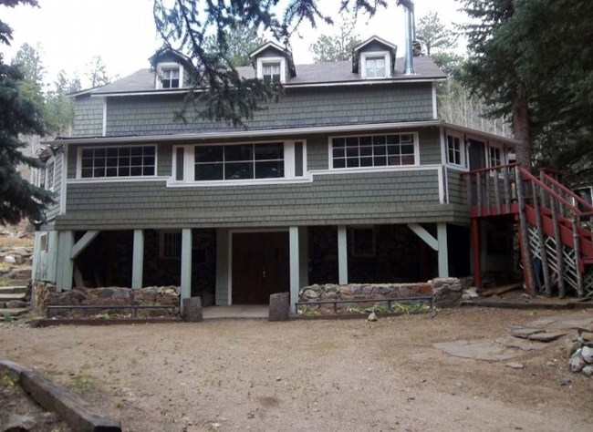 Three story wooden house with an entrance through the basement. The house is painted green and has stairs leading tot he landscape from the sides of the house