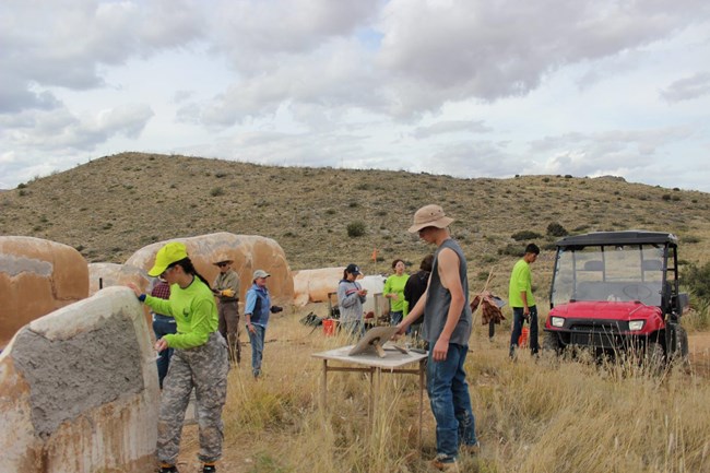 Two students from the Arizona Youth Summit add mud to the wall of the Post Trader's Store as a part of their field school experience.  Other youth summit participants and instructors can be seen in the background.
