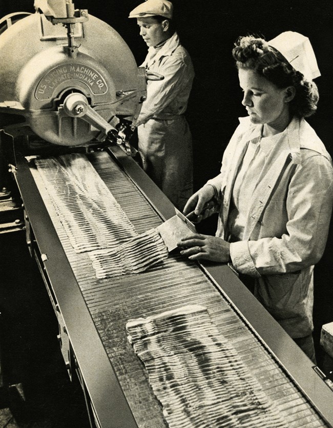 Black and white photograph of a female and male worker on an assembly line packing bacon