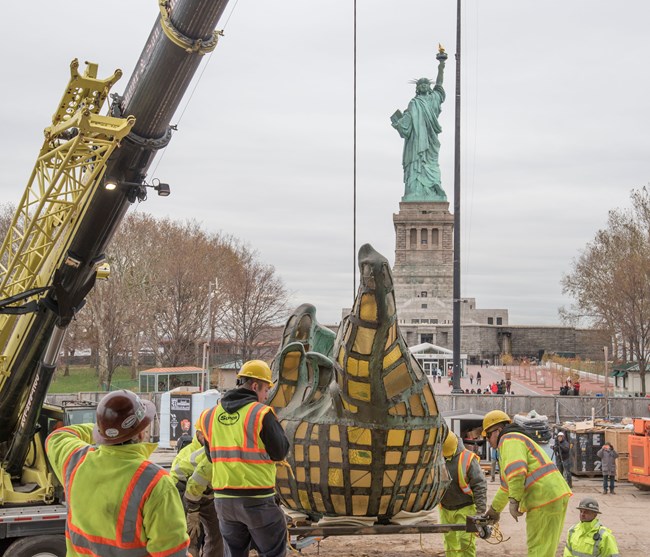 The original torch being lifted by crane with the Statue of Liberty in the background.