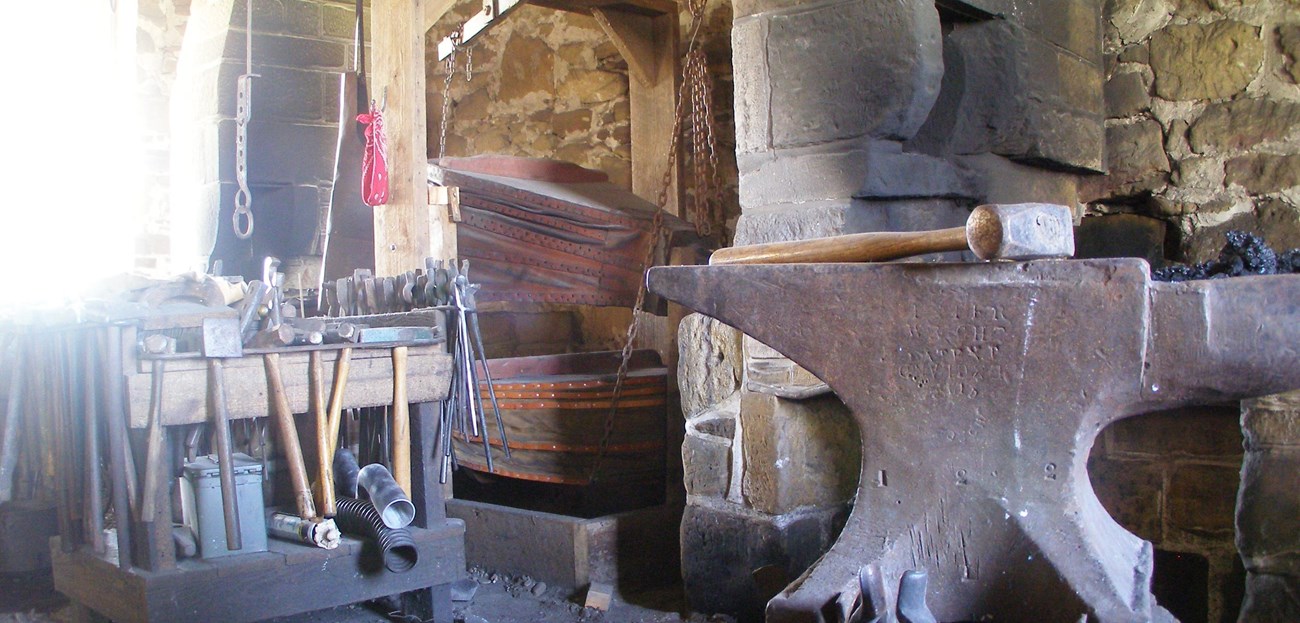 19th century blacksmith shop, anvil in foreground, forge in background.