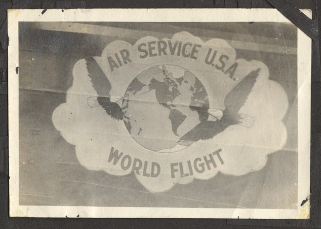 Black and white photo of logo with a globe and two eagles. Text around the image reads "Air Service U.S.A. World Flight"