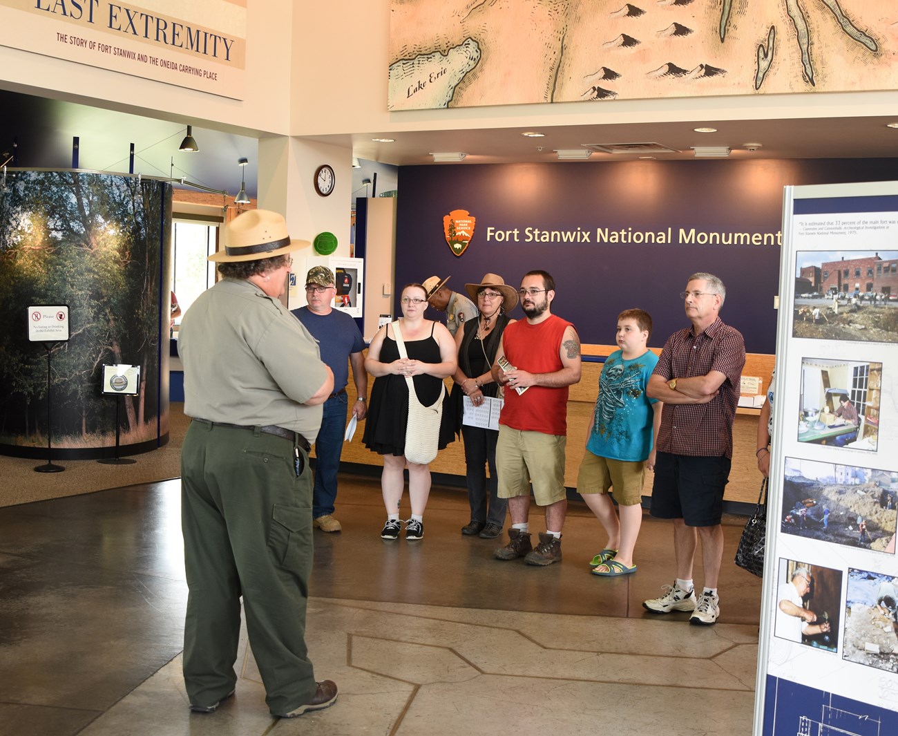 a park ranger stands in front of a colorful crowd at a visitor center, and points at a map.