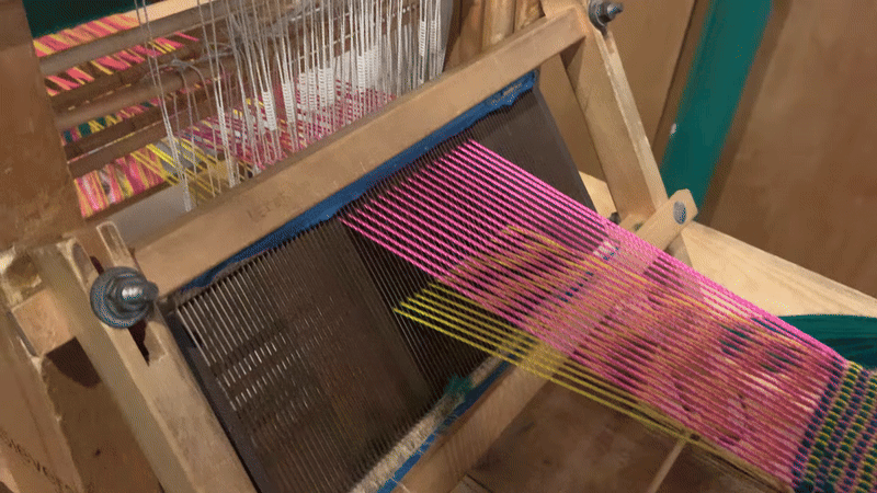 pink and yellow yarns laid out in a row are alternatingly lifted up and down