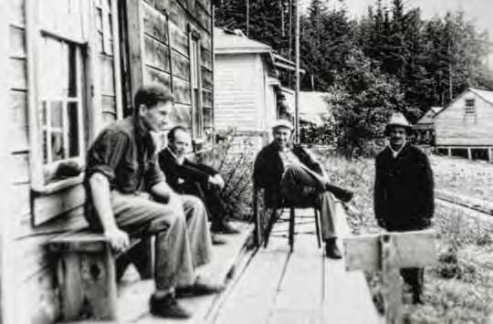 Black and white photo of four men gathered on a rough wood porch.
