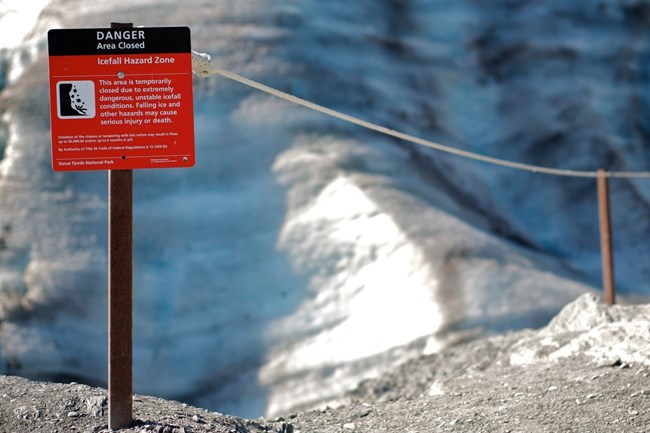 A red warning sign next to a roped area, in front of ice from a glacier.
