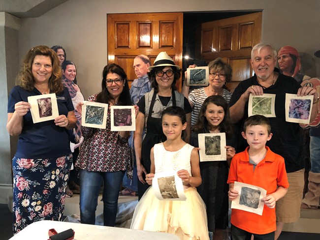 Sabra and her students hold up their prints after the public printmaking workshop in the Visitor Center.