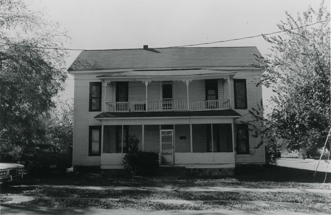two story symmetrical house with a screen porch on the ground level and an open porch on the second level.