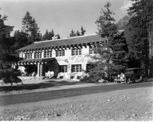 Long two-story historic building with many windows sits nestled in trees.