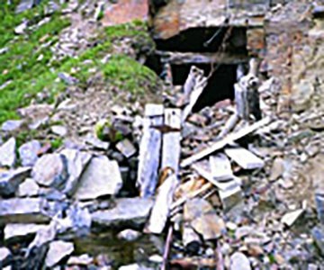 An abandoned mine cut in the side of a mountain with discarded timber and steel.