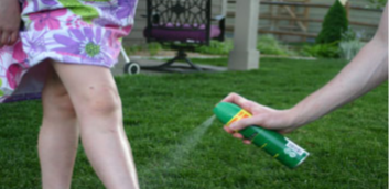 One person sprays bug spray on the legs of another person