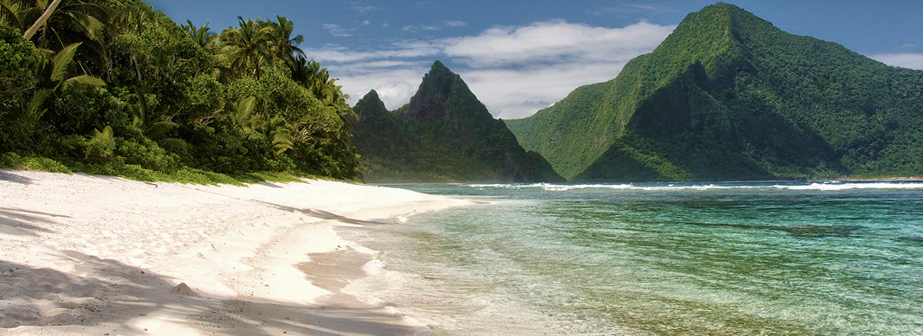 Sandy beach and turquoise waters with forested tropical mountain in distance