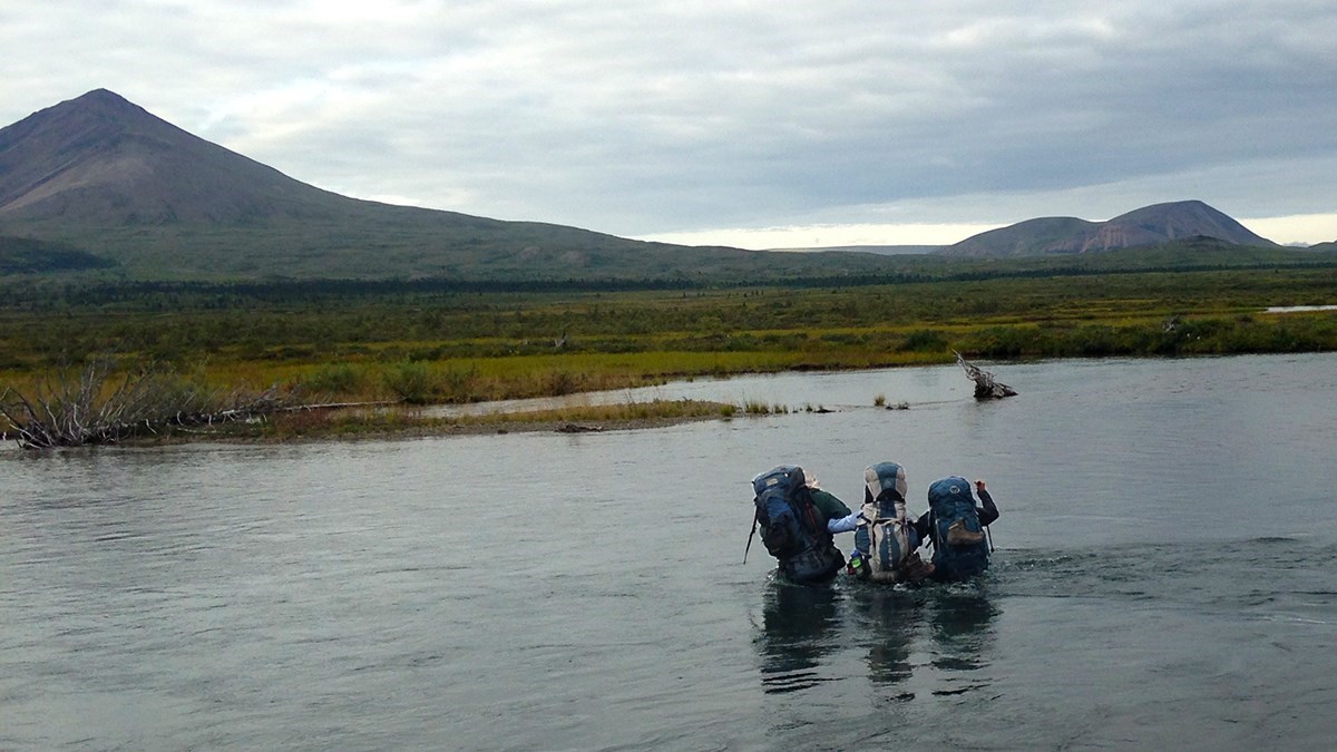 3 backpackers cross a waist deep river