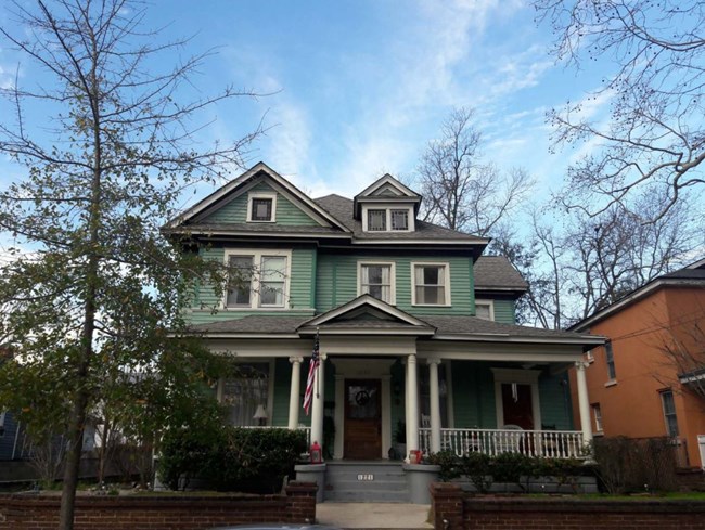 three store house with a front porch and supporting columns and stairs walking up to the front door.