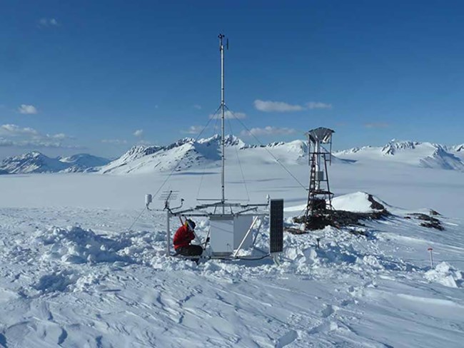 A scientist works on weather station equipment high in the snow-covered mountains.