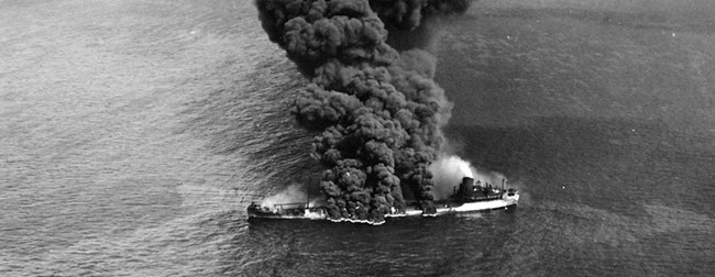 A ship burns with thick black smoke.
