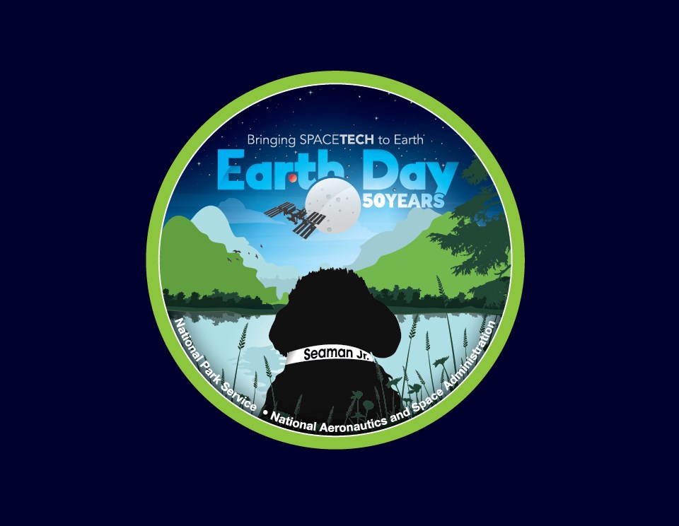 A green circle that contains a black dog named Seaman, a space station, with the words Earth Day 50 years.