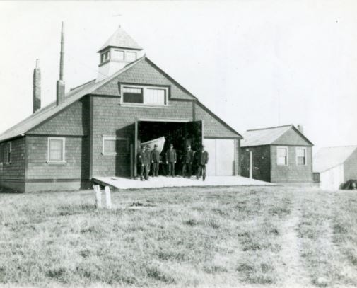 Coast Guard men stand in front of an open garage door.