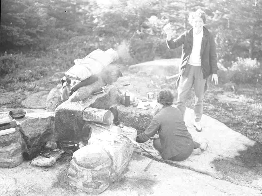 B&W photo of two individuals next to stone fire pit with smoke