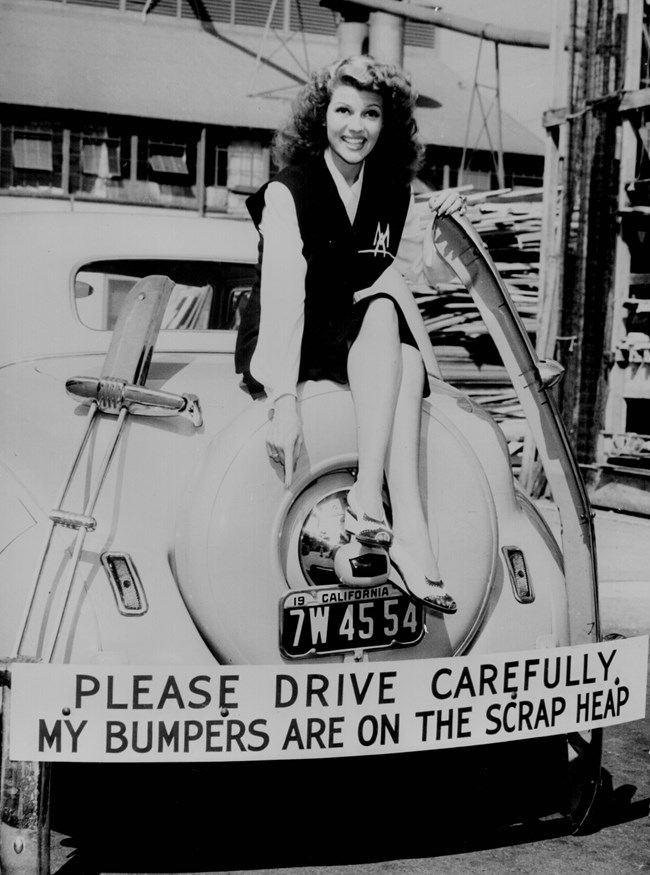 Woman sitting on a car whose bumpers were donated to the war effort