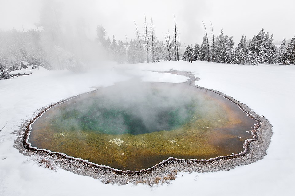 A colorful thermal pool surrounded by white snow