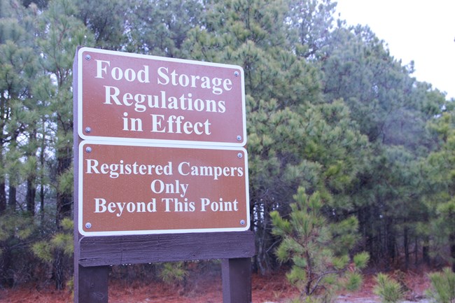 Two large brown signes, one reading: "Food storage regulations in effect", and another reading "Registered campers only beyond this point"