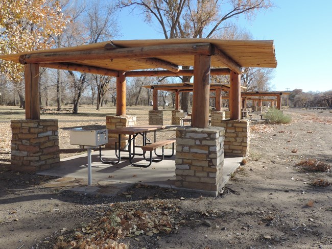 A shade structure in a picnic area with a table and grill.