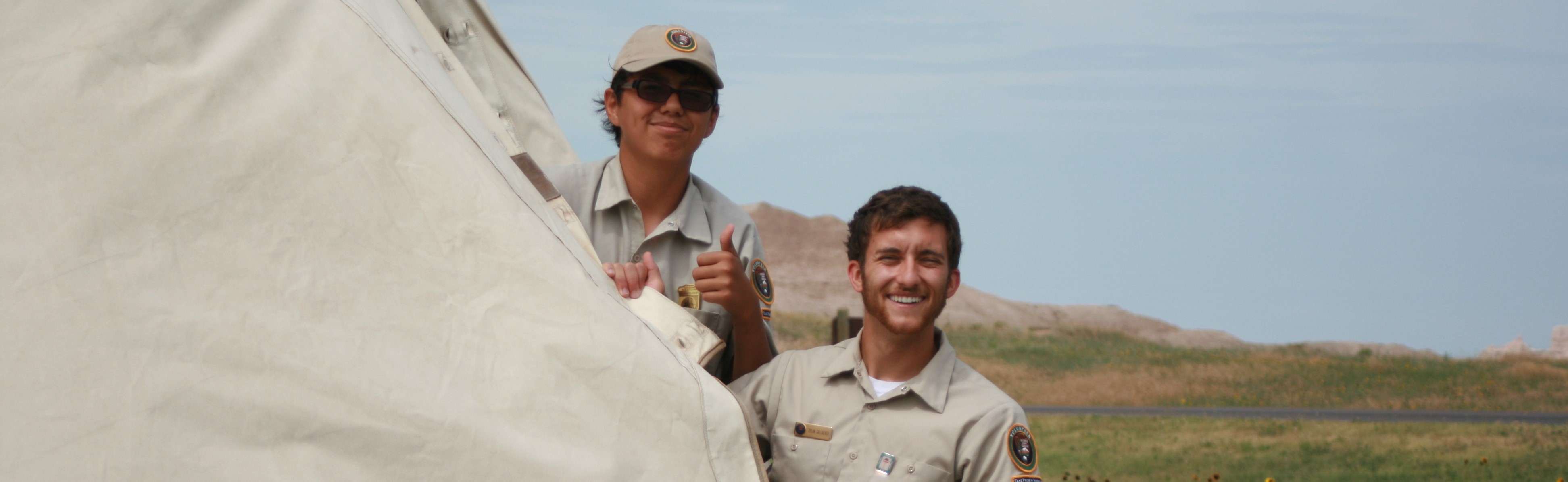 two men in volunteer uniforms pull a sheet of canvas to the right.