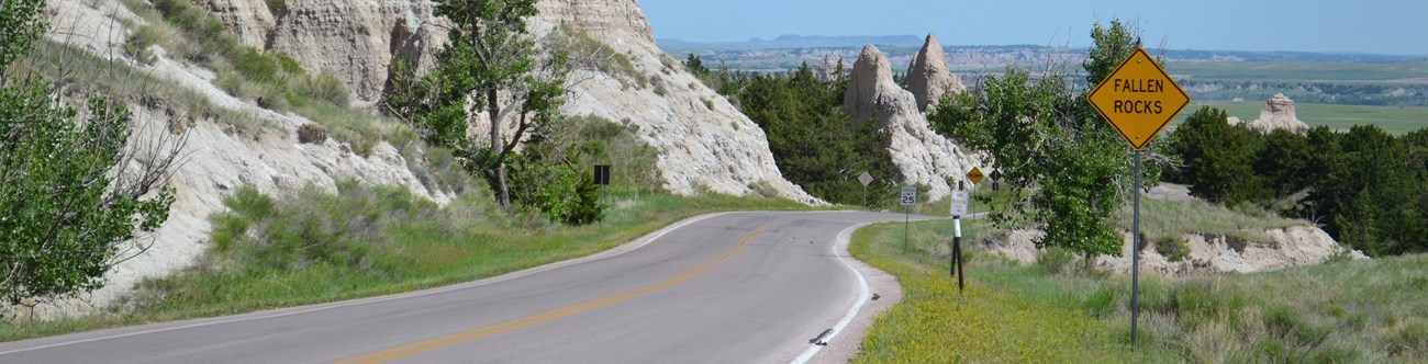 a road winds between badlands formations with a yellow sign on the right that says fallen rocks.