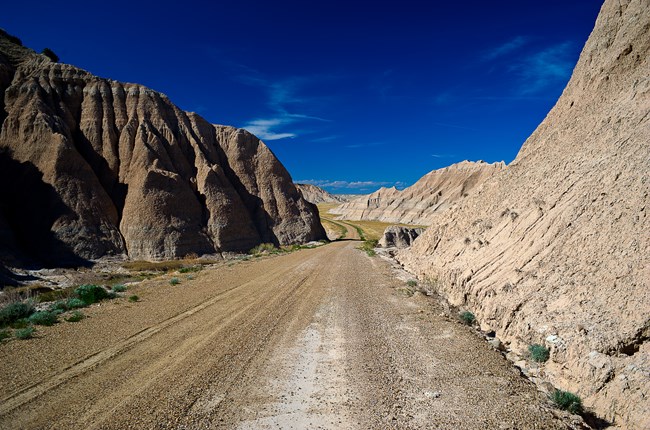 Image of gravel road going through pass at Sheep Mountain Table, with jagged Badlands rock formations.