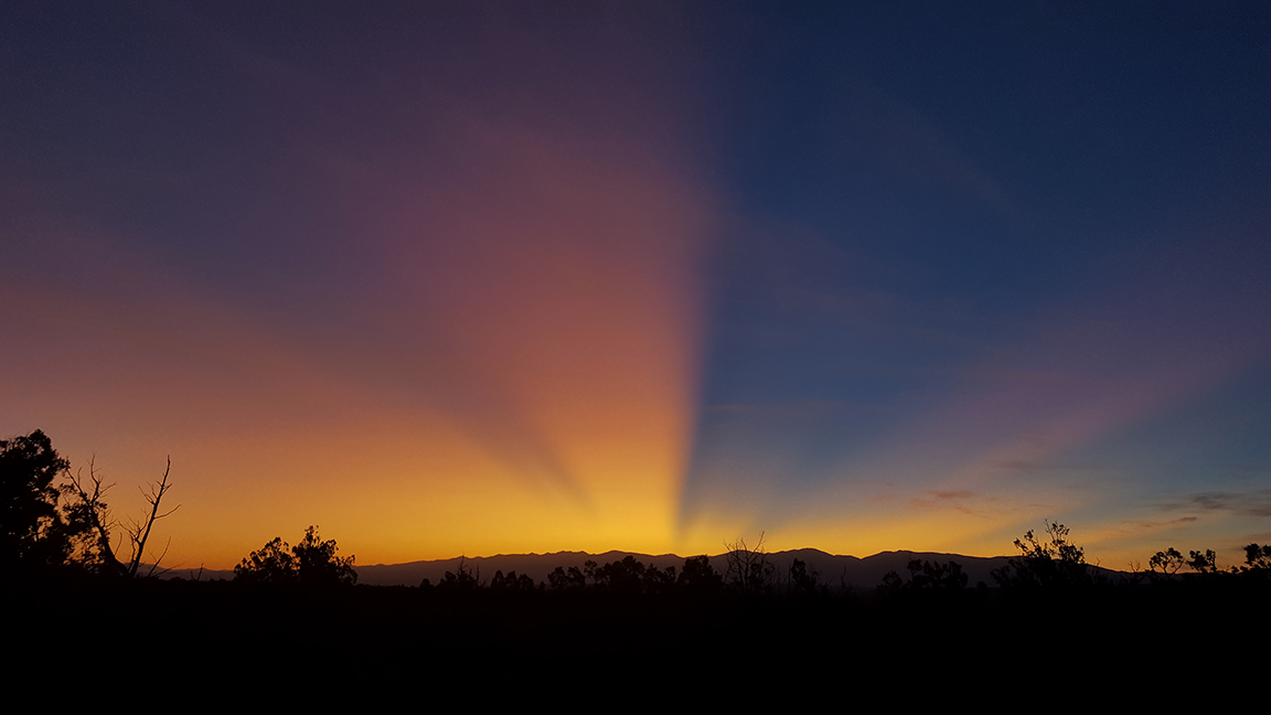The sun rises over a mountainside.