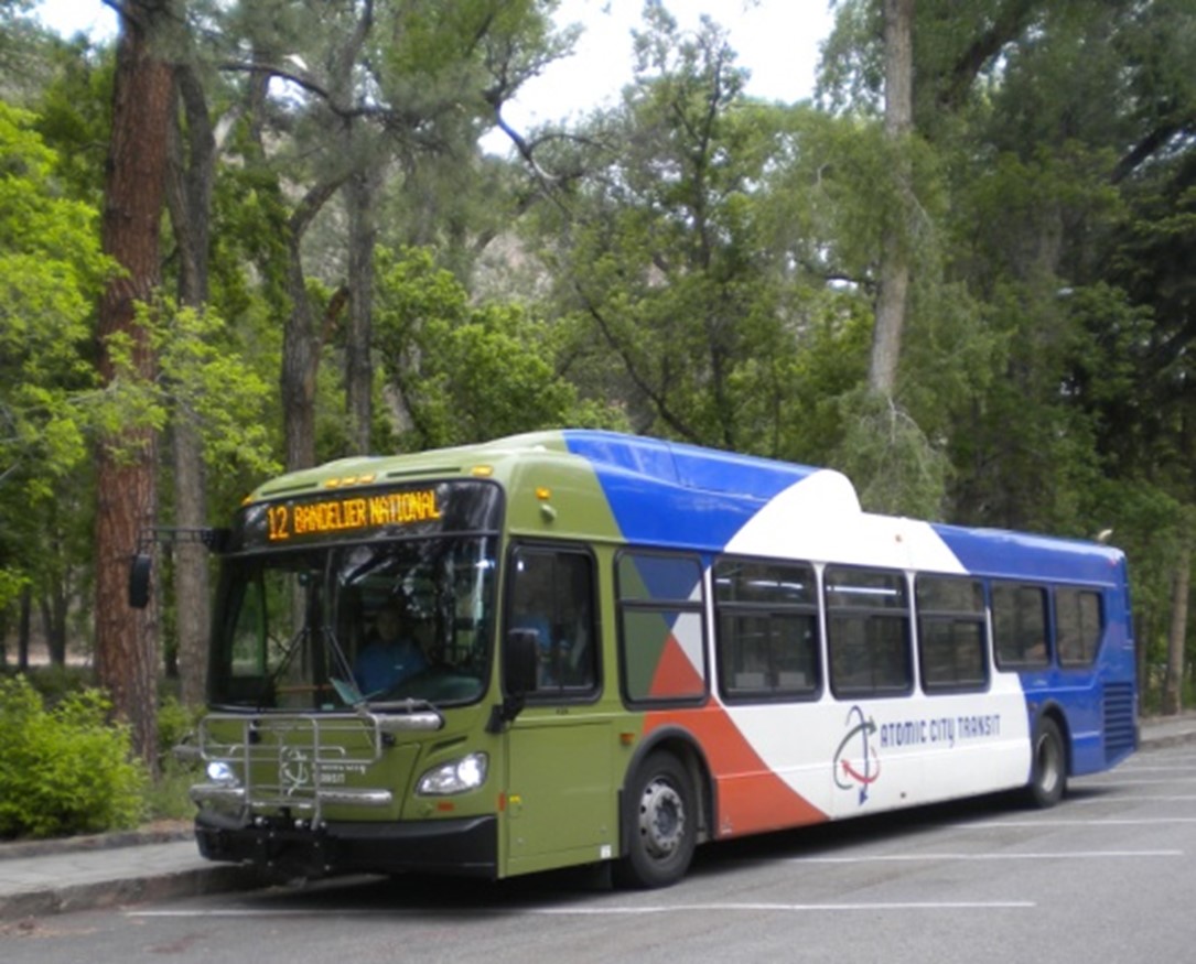 A multi-colored shuttle bus in a forested parking lot