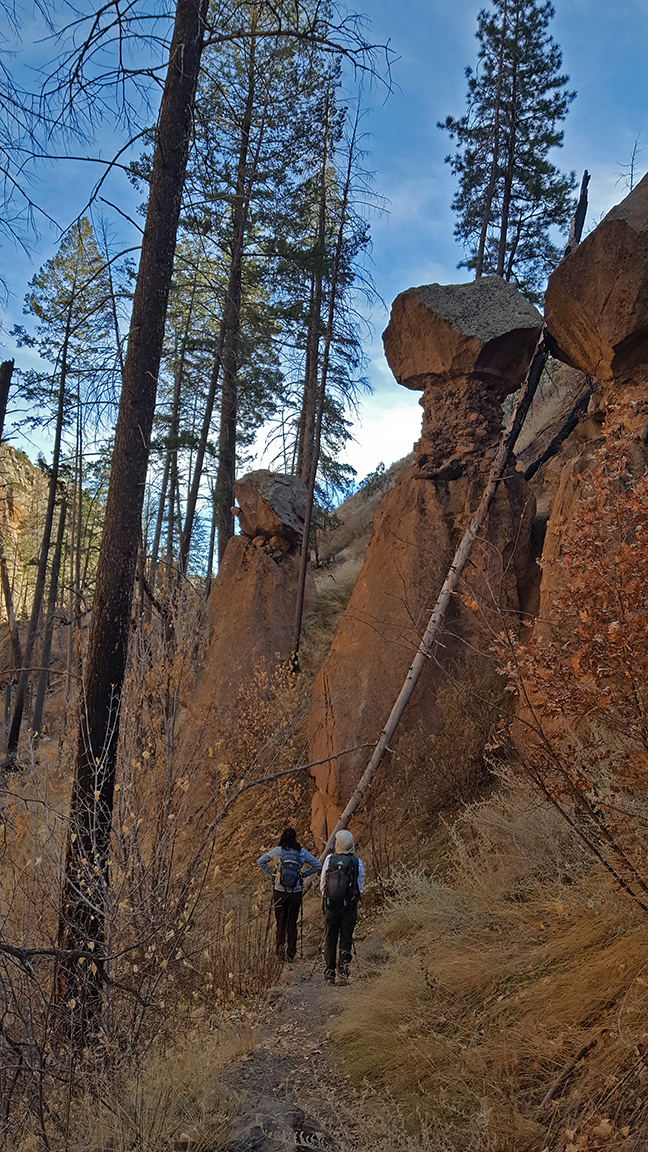 tent shaped reddish rock forms tower above two people