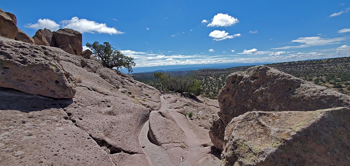 a trail carved into the rock crosses a mesa with views of mountains behind