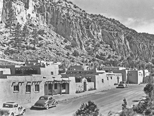 A black and white image of stone buildings and old cars in a canyon.